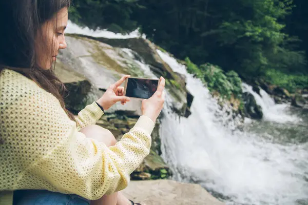 Woman taking picture on the phone of waterfall on background — Stock Photo, Image