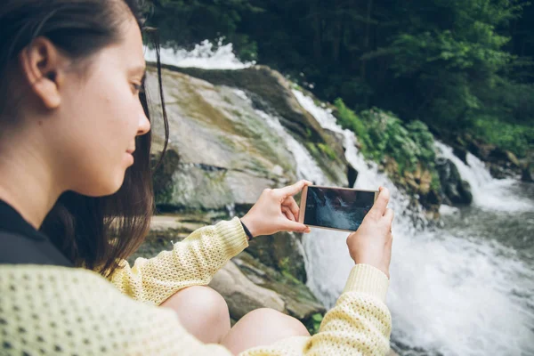 Woman taking picture on the phone of waterfall on background — Stock Photo, Image