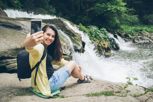 女性の背景に滝の携帯電話で写真を撮る — ストック写真