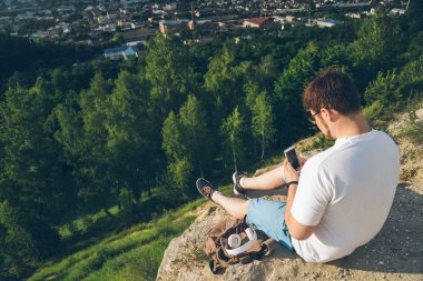 telefon ile tepe üzerinde oturan adam