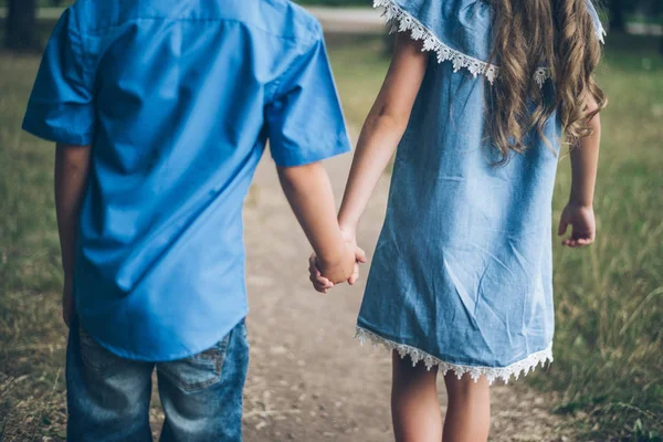 Ein kleiner Junge und ein kleines Mädchen gehen zusammen und halten sich an den Händen — Stockfoto