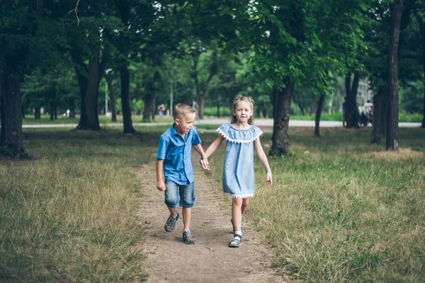 Ein kleiner Junge und ein kleines Mädchen gehen zusammen und halten sich an den Händen — Stockfoto