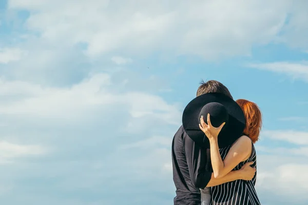 Mulher beijo namorado enquanto se esconde atrás do chapéu — Fotografia de Stock