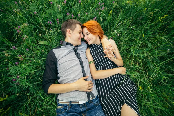 Young happy beautiful couple man and woman lying outdoors on the bright sunny day on green lawn — Stock Photo, Image