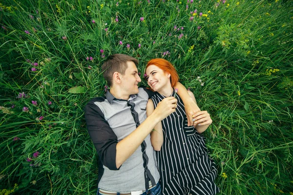 Genç mutlu güzel çift erkek ve kadın açık havada parlak güneşli günde yeşil çim üzerinde yalan — Stok fotoğraf
