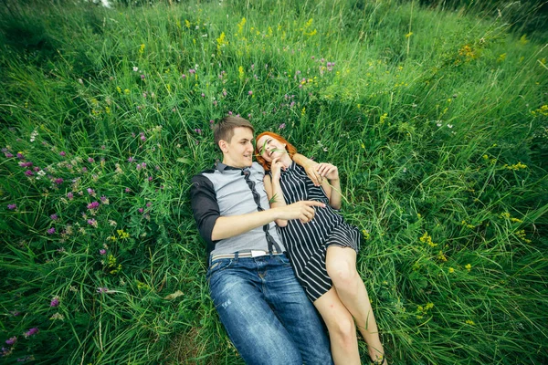 Unga glada vackra par man och kvinna ligga utomhus på en solig dag på grön gräsmatta — Stockfoto