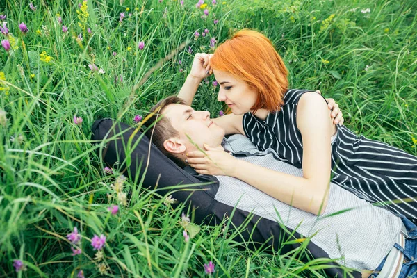 Unga glada vackra par man och kvinna ligga utomhus på en solig dag på grön gräsmatta — Stockfoto