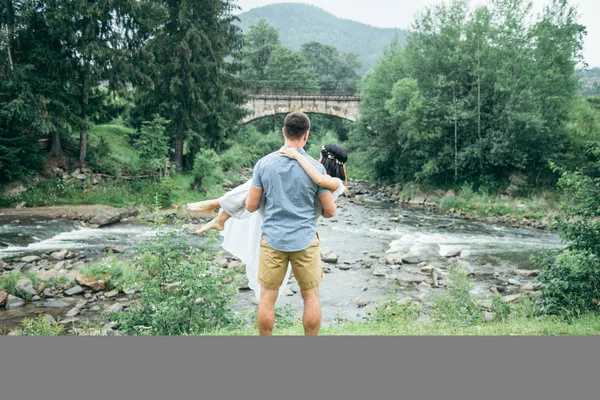 Mann nimmt Frau in der Nähe von Gebirgsfluss auf den Arm — Stockfoto
