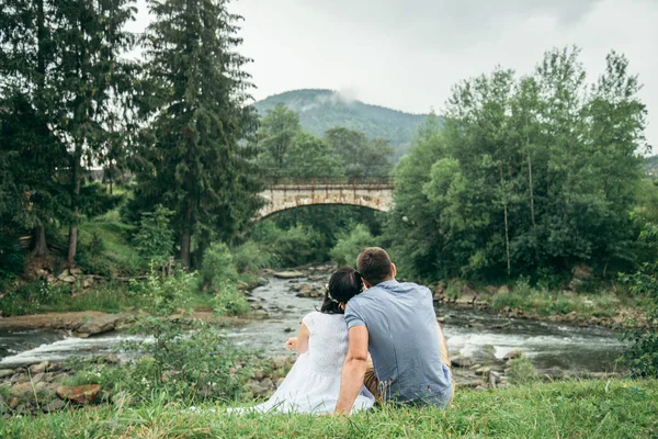 couple sits near mountain river