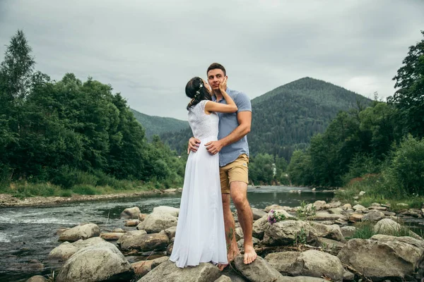 Пара стоит возле горной реки с горами на заднем плане — стоковое фото