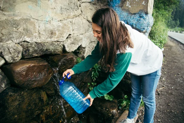 Giovane donna riempire la bottiglia da montagne fonte d'acqua — Foto Stock