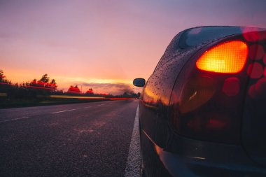 yolda yağmurla yan yolda araba ile kırmızı günbatımı