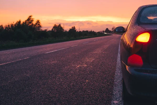 yolda yağmurla yan yolda araba ile kırmızı günbatımı