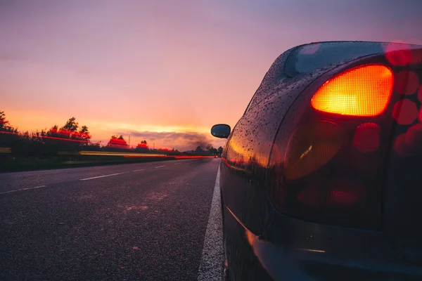 Röd solnedgång med regn på vägen med bilen på sida vägen — Stockfoto