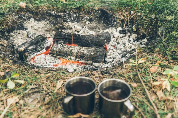 Två metall koppar med te nära bonfire — Stockfoto