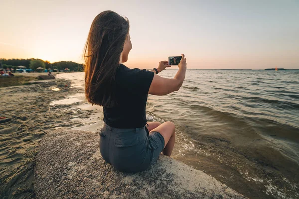 Frau sitzt am Strand und fotografiert das Meer — Stockfoto