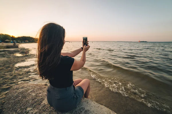 Woman sits on a beach and takes picture of the seaside — Stock Photo, Image