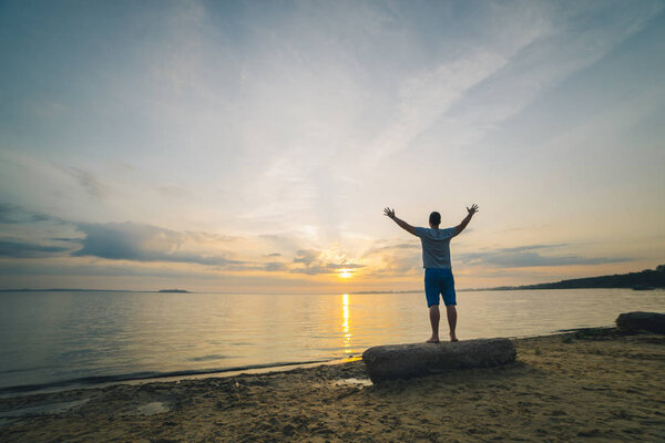 мужчина на пляже смотрит на восход солнца с поднятыми руками
