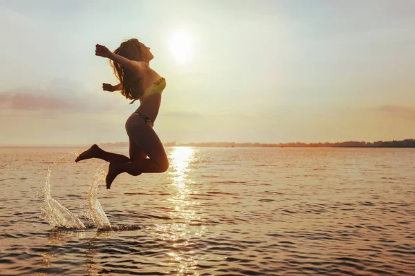 Young Woman Jumps on Beach at sunset