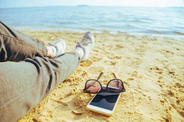 kadının ayak plaj üzerinde güneş gözlüğü ile cep telefonları ona yakın: