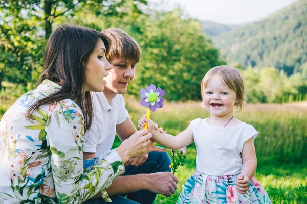 Genitori giocano con la figlia sul campo con le montagne sullo sfondo — Foto Stock