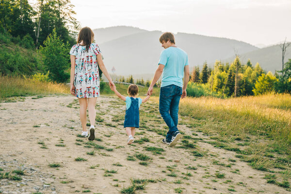 mother and father holding daughter hands and walking by mountains