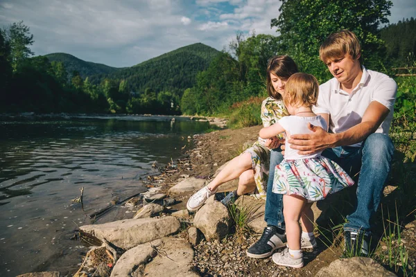 Молода сім'я сидить біля гірської річки зі своєю дочкою — стокове фото