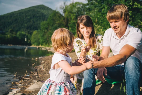 Familia joven se sienta cerca del río de montaña con su hija —  Fotos de Stock