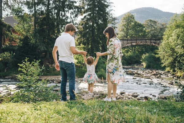 Feliz familia jugar con hija cerca del río en las montañas —  Fotos de Stock