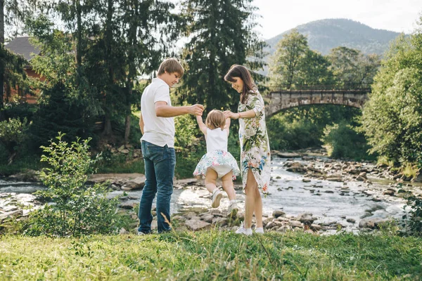Щаслива родина грає з дочкою біля річки в горах — стокове фото