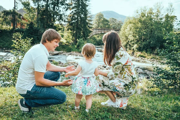 Щаслива родина грає з дочкою біля річки в горах — стокове фото