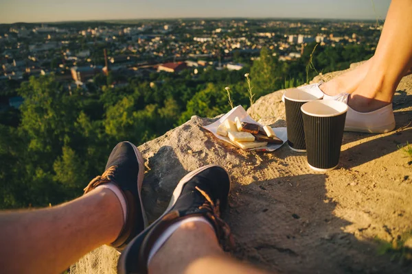 Man and woman legs on the top of the hill with two cups and chocolate — Stock Photo, Image