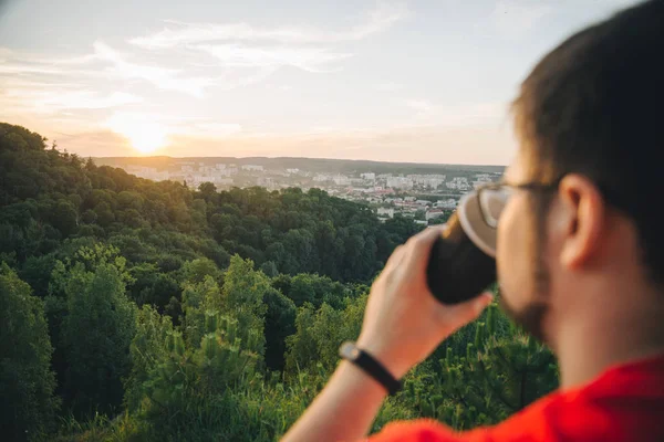 Человек, сидящий на вершине холма с чашкой кофе — стоковое фото