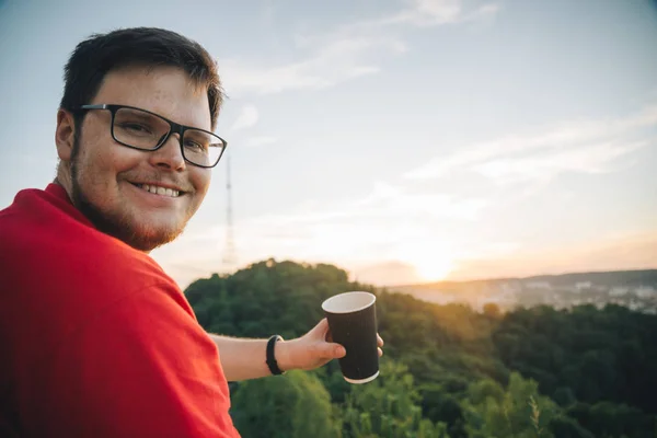 Человек, сидящий на вершине холма с чашкой кофе — стоковое фото