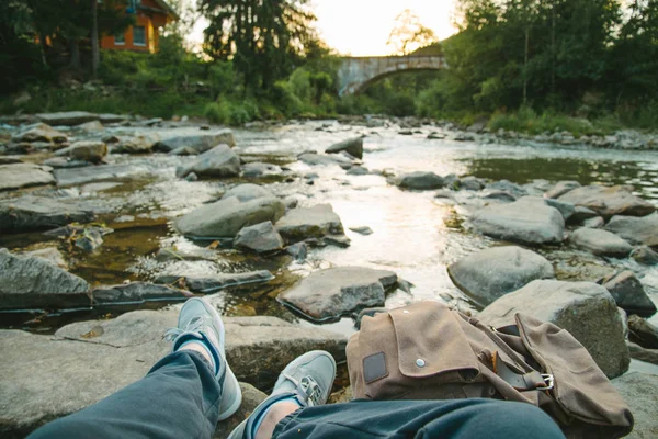 L'uomo siede vicino al fiume di montagna guardando il tramonto — Foto Stock