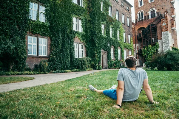 Homem sentado no chão no parque da cidade e olhando para o edifício velho — Fotografia de Stock