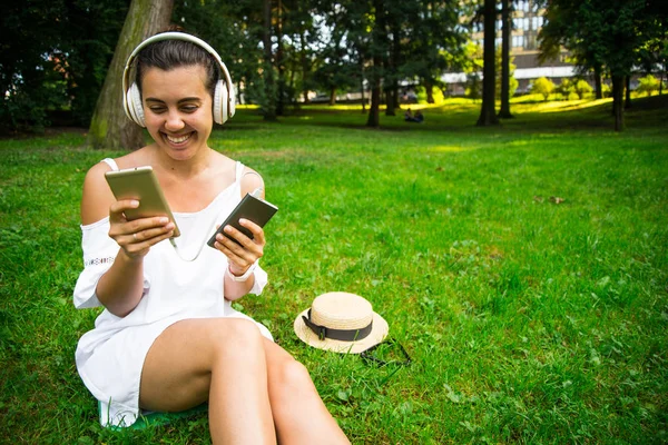 Жінка в парку з радістю користується павербанком і продовжує слухати музику — стокове фото