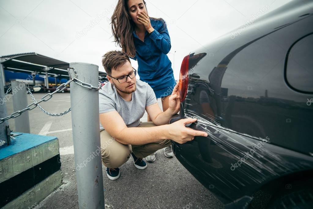 sad man looking on car scratch, woman stand behind him