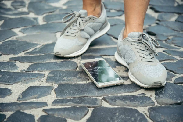 Pantalla de teléfono inteligente agrietado cerca de piernas —  Fotos de Stock
