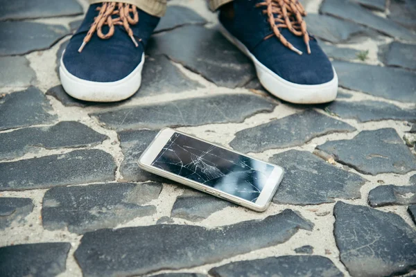 Cracked smartphone screen near legs — Stock Photo, Image