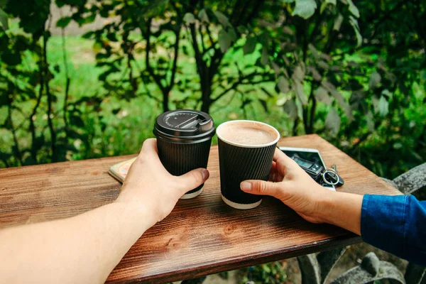 Two hands hold cups of coffee on the wooden table — Stock Photo, Image