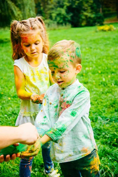 Niños pequeños emocionales jugando con pinturas holi en el parque de la ciudad —  Fotos de Stock
