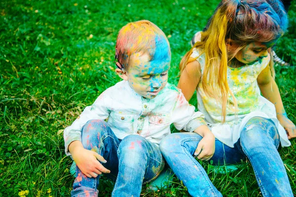 Niña con niño sentarse en el suelo todo sucio en pinturas holi — Foto de Stock