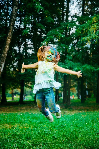 Retrato de niña feliz, toda la cara en pinturas holi — Foto de Stock