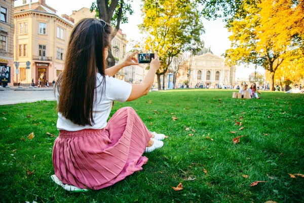 Woman sitting on th grass and taking picture of old beuilding — Stock Photo, Image