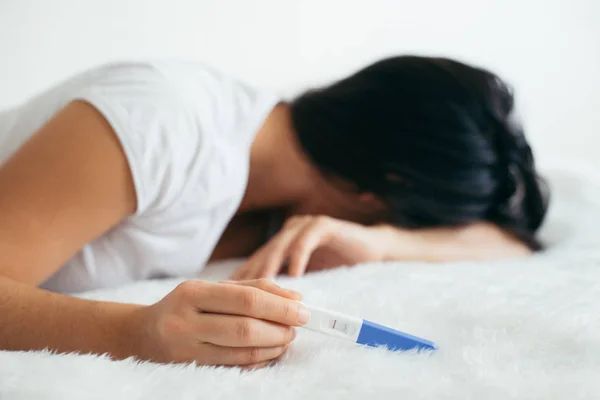 Mujer molesta se acuesta triste en la cama con la prueba de embarazo negativa — Foto de Stock