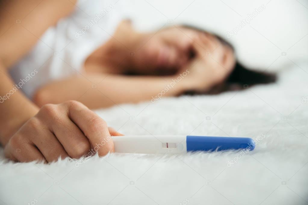 Upset woman lie sad in the bed with negative pregnancy test