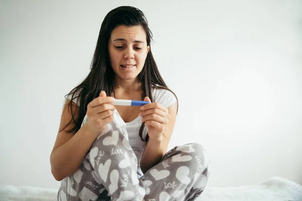 Kvinna i sängen överraskad av graviditetstest — Stockfoto
