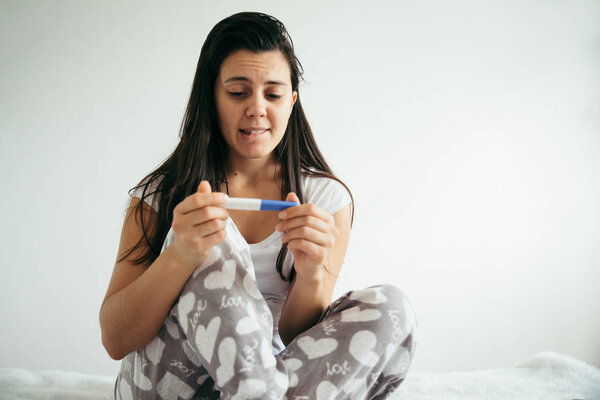 женщина в постели удивлена тестом на беременность
