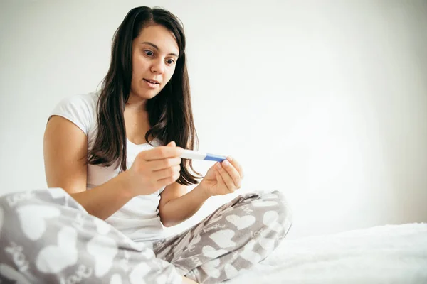 Kvinna i sängen överraskad av graviditetstest — Stockfoto